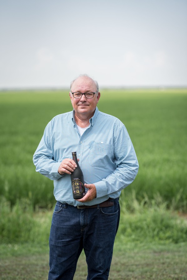 Chris Isbell stands near his rice fields holding a bottle of sake. 